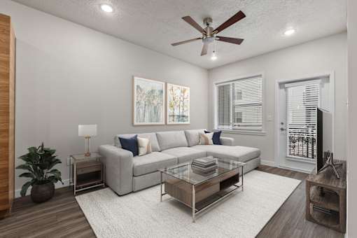 A living room with a grey couch, a glass coffee table, and a ceiling fan.