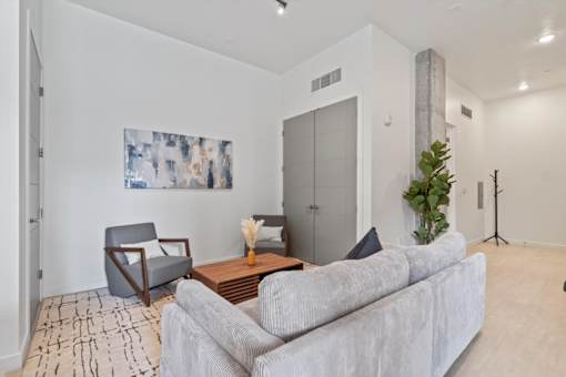 A living room with a grey couch, a grey armchair, a wooden coffee table, and a painting on the wall.