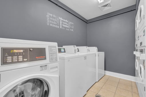 washing machines and dryers in a laundry room with a gray wall and gray walls at AVIA Lofts on Liberty Ridge, Jacksonville, FL, 32256