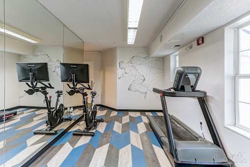 A treadmill and two stationary bikes are in a room with a world map on the wall.