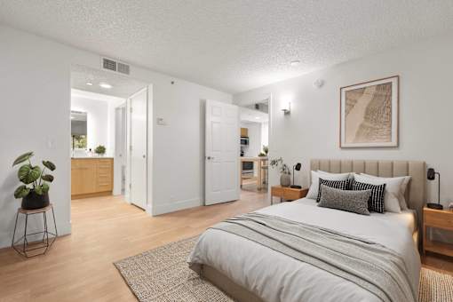 A bedroom with a large bed and a plant on a stand.