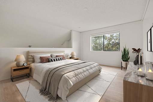 A well-lit bedroom with a large bed and a window showing greenery outside.