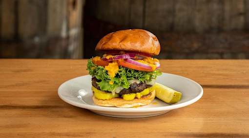 A burger with lettuce, tomato, pickles, and onions is on a plate.