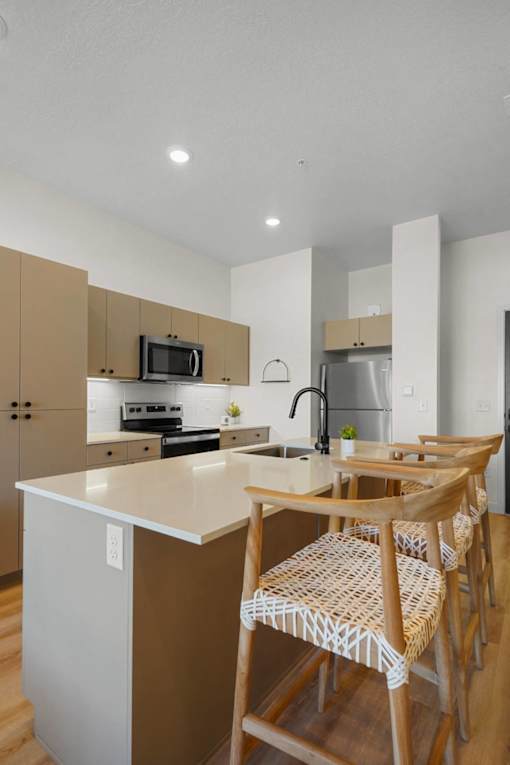 A kitchen with a white counter top and wooden chairs.