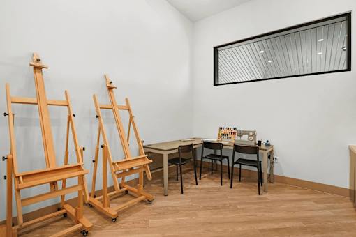 Two wooden easels stand in front of a table with a mirror on the wall.