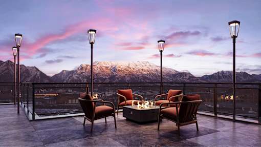 A table with chairs and a lamp on a balcony overlooking a mountain range.