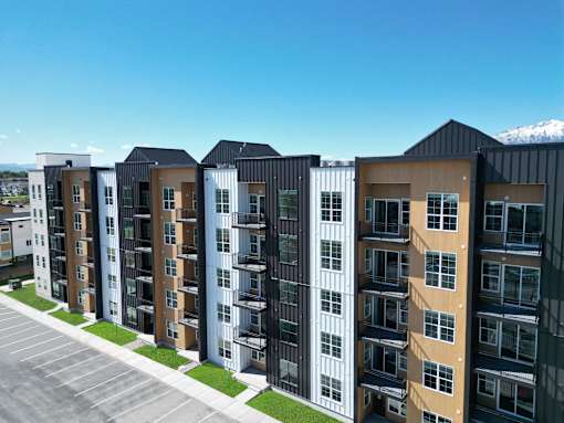 A row of modern apartment buildings with a parking lot in front.