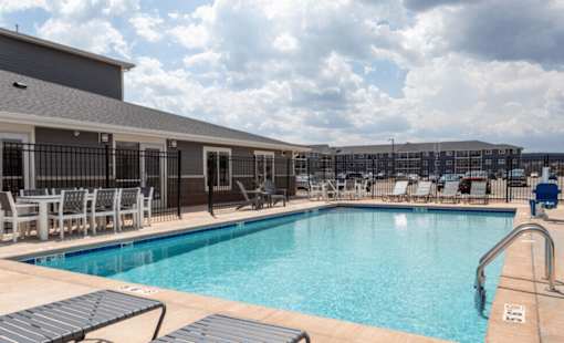 a swimming pool with lounge chairs and tables and a building in the background at Red Rock Apartments, Rapid City, South Dakota