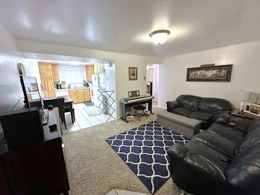 A living room with a black leather couch and a rug.