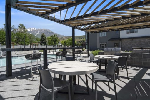 a patio with tables and chairs with a pool and mountains in the background at The Flats at Riverwoods, Provo, Utah