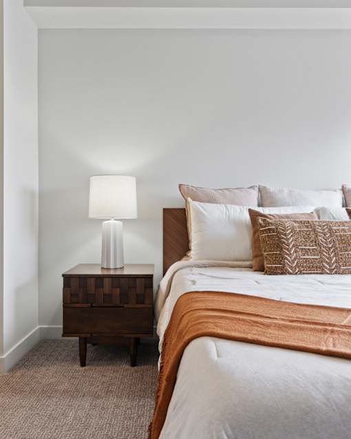 A bed with a white comforter and a lamp on a side table at Wilmington Flats Apartments, Salt Lake City, UT