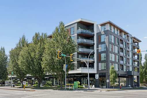 A modern multi-story building with balconies is situated on a street corner with a traffic light.