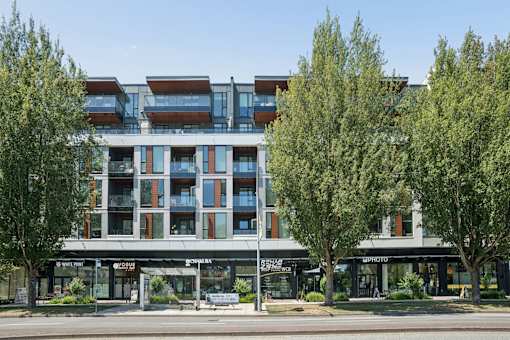 A modern building with a glass facade and trees in front.