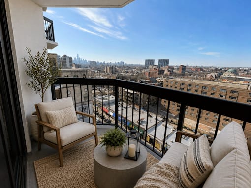 A balcony with a chair, cushions and a table with a plant and candle.