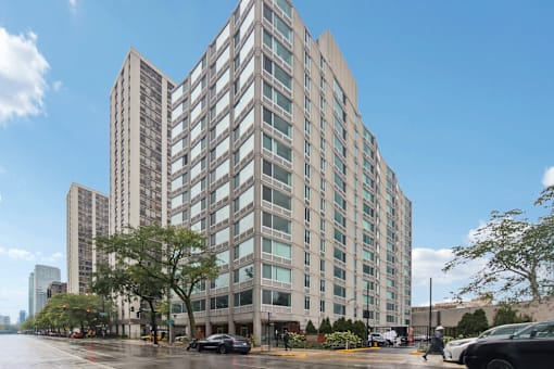 A tall building with many windows is in the middle of a city street.