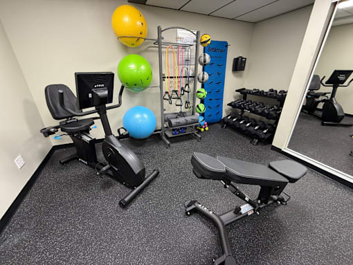 A gym room with a variety of equipment including a stationary bike, a bench, and a mirror.