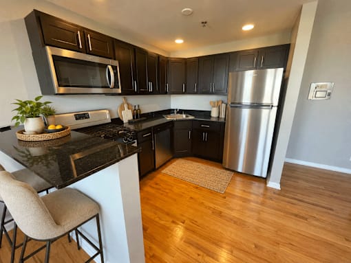 A kitchen with a black counter top and a stainless steel refrigerator.
