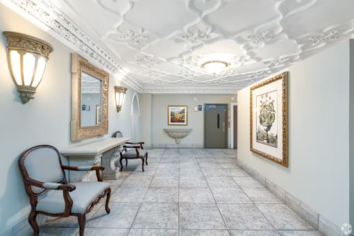 A hallway with a chair, a table, and a painting on the wall.