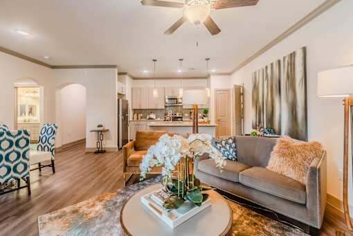 A living room with a grey couch and a coffee table with a vase of flowers on it at Atlas Point at Prestonwood Apartments , Texas, 75010
