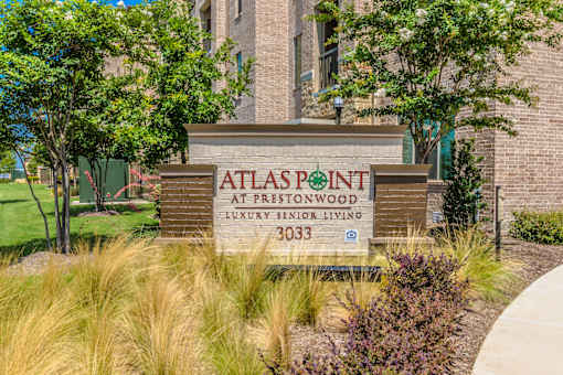 A sign for Atlaspoint at Prestonwood, a luxury senior living community, is displayed in front of a brick building at Atlas Point at Prestonwood Apartments , Carrollton, Texas