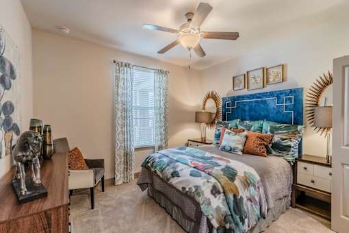 A bedroom with a bed, a chair, a nightstand, and a ceiling fan at Atlas Point at Prestonwood Apartments , Texas