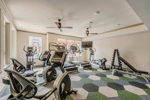 A spacious gym with a variety of equipment including treadmills, elliptical machines, and a rowing machine. at Atlas Point at Prestonwood Apartments , Texas