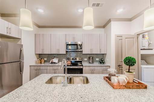 A modern kitchen with a granite countertop and stainless steel appliances at Atlas Point at Prestonwood Apartments , Carrollton, TX