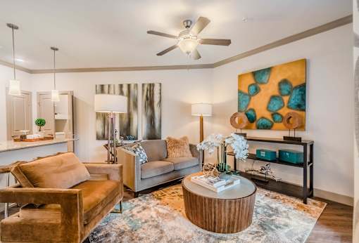 A living room with a brown leather chair, a grey sofa, a wooden coffee table, and a painting on the wall at Atlas Point at Prestonwood Apartments , Carrollton