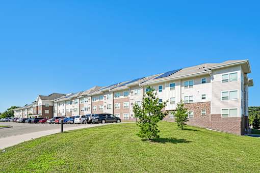 A row of apartment buildings with cars parked in front.