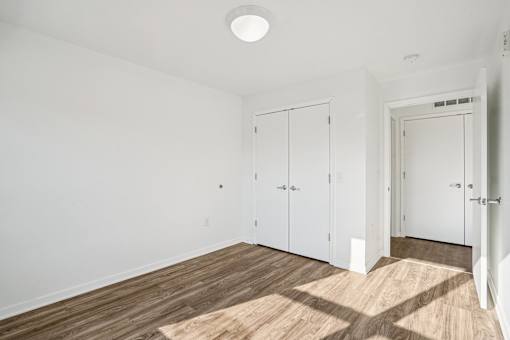 A room with white walls and wooden flooring with a door and two cabinets.