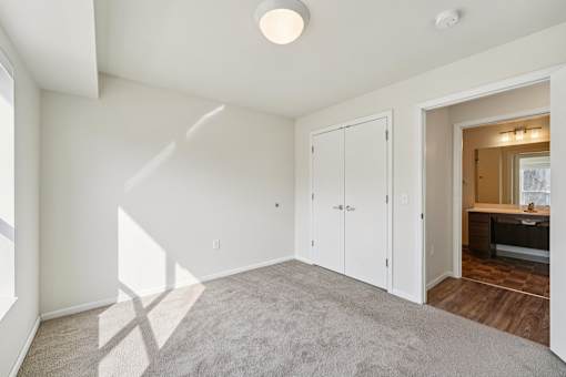 A room with white walls and a carpeted floor with a white door and a window.