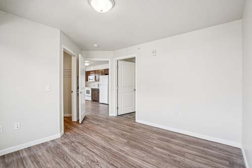 A room with white walls and wood flooring with a doorway leading to another room.