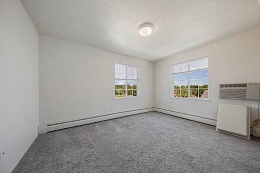 A room with a carpeted floor and two windows.