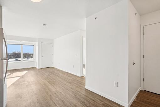 A white room with wood flooring and a window.