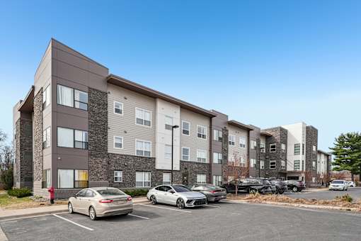 A parking lot in front of a multi-story apartment building with cars parked.
