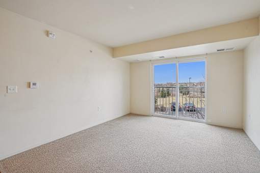 A large empty room with a carpeted floor and sliding glass doors.