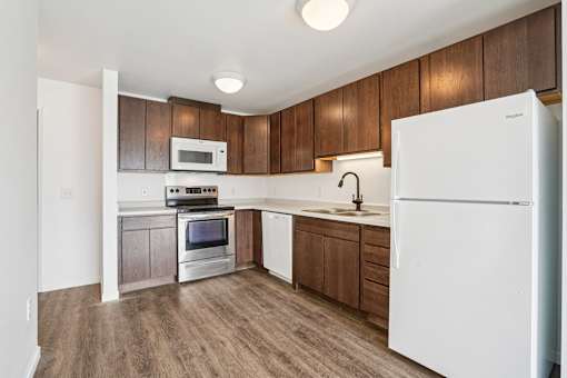 A white refrigerator is in the corner of a kitchen with wooden cabinets.