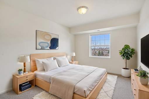 A bedroom with a large bed, a nightstand with a lamp, and a painting on the wall.