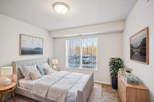 A bedroom with a large bed, a nightstand, and a window with blinds.