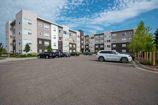 A parking lot in front of a multi-story apartment building with cars parked.