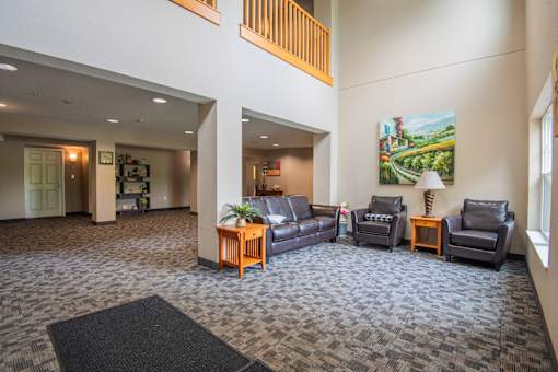A living room with a grey carpet and a painting on the wall.