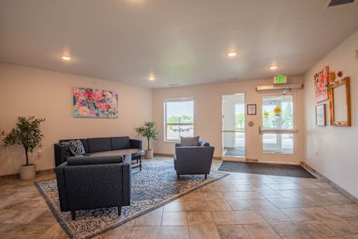 A spacious living room with a black sofa set and a rug in the middle.