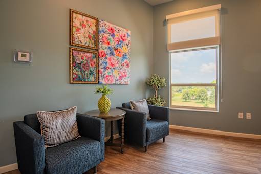 A living room with two chairs, a table, and a painting on the wall.