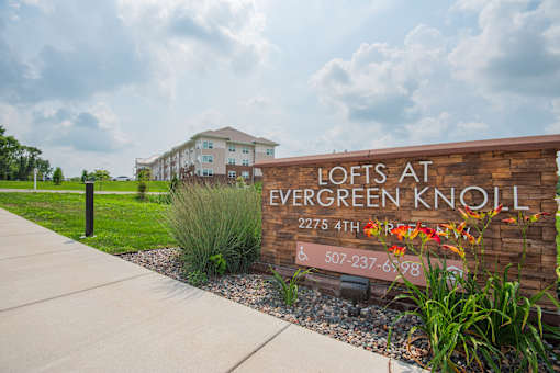 A brick sign that says Lofts at Evergreen Knoll in front of a building.
