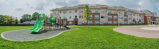 A playground with a green slide in front of a large building.