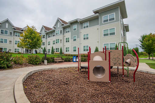 A playground with a slide and a tunnel in front of apartment buildings.