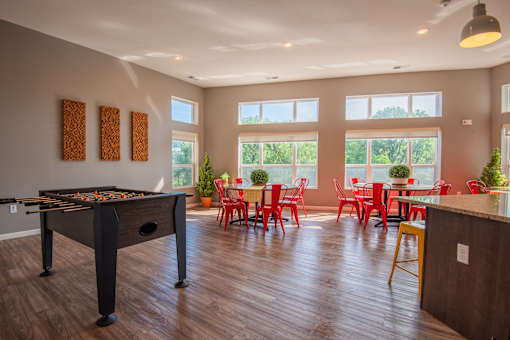 A foosball table is in the middle of a room with red chairs and tables.
