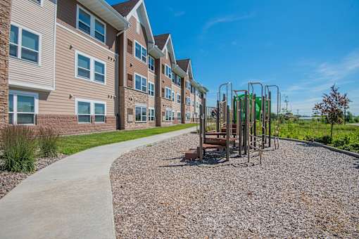 A playground with a swing set is located in front of a building with a paved walkway.