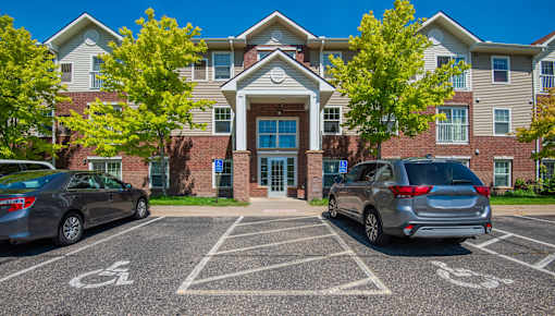 A parking lot in front of a building with cars parked and a handicap sign on the ground.