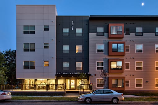 A modern apartment building named Thomas Avenue is shown with a car parked in front.